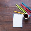 photo of notebook with pencil, cup of coffee and colorful pencils on the wonderful brown wooden background
